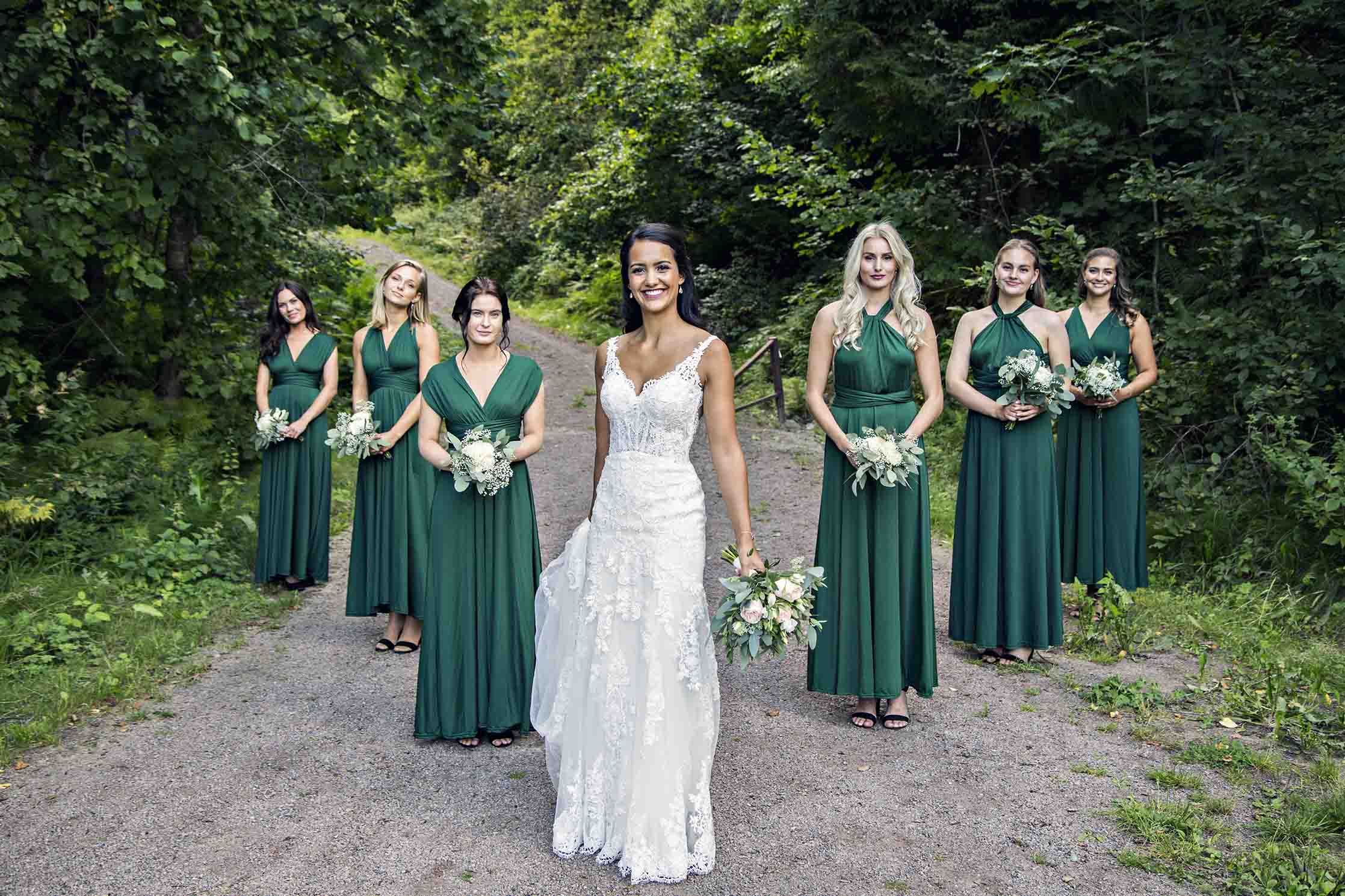 Brud i hvit tettsittende blondekjole med slep, enkel brudebukett og løst hår. Brudepiker i grønne kjoler. Forlovelseskjoler.