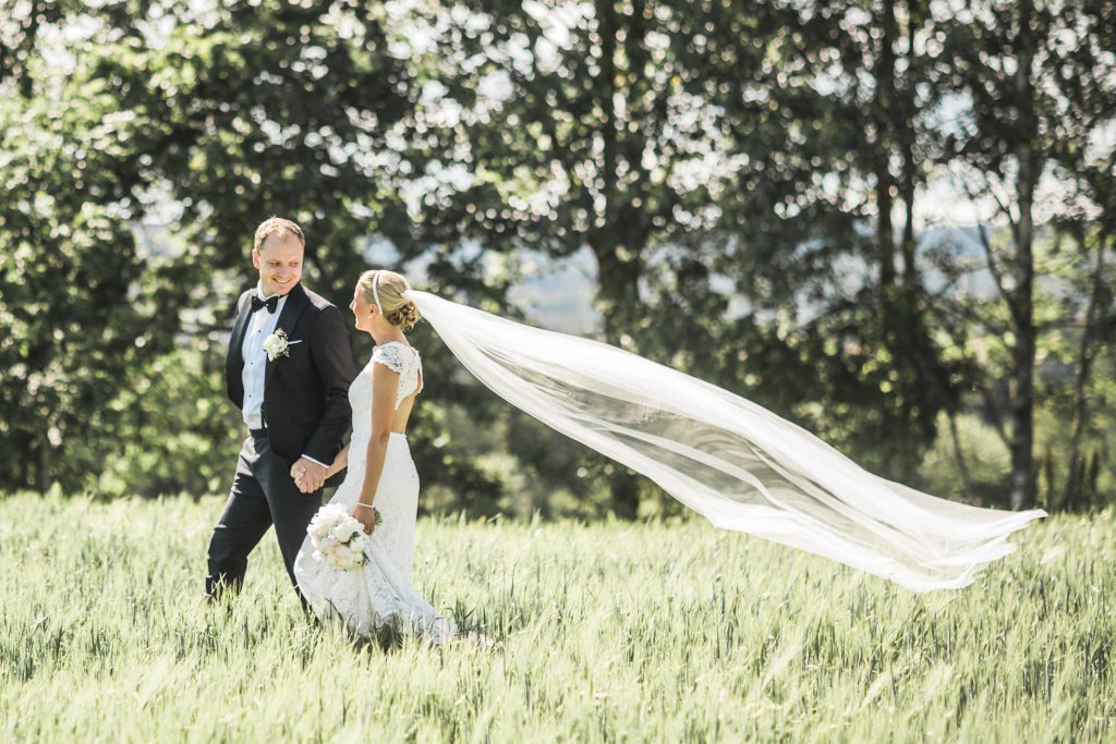 Brudepar løpende i høyt gress. Brud har hvit brudekjole og langt slør. 