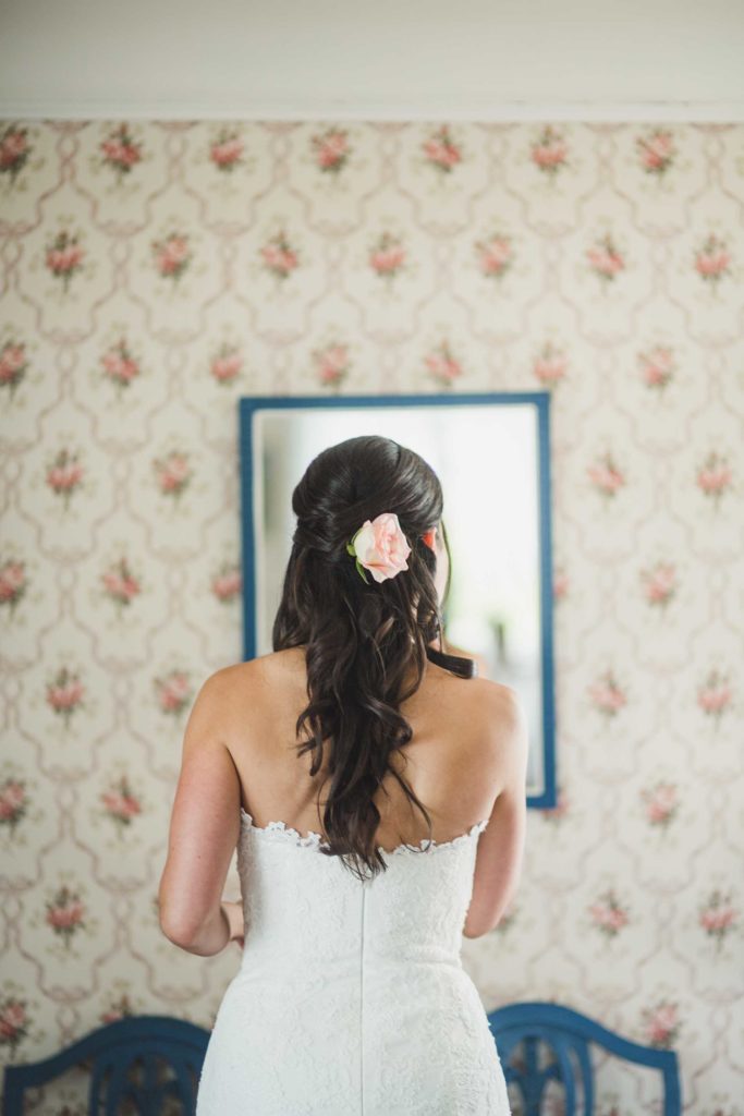 Brud gjør seg klar på bryllupsdagen med hvit brudekjole og blomst i krøllete mørkt langt hår.