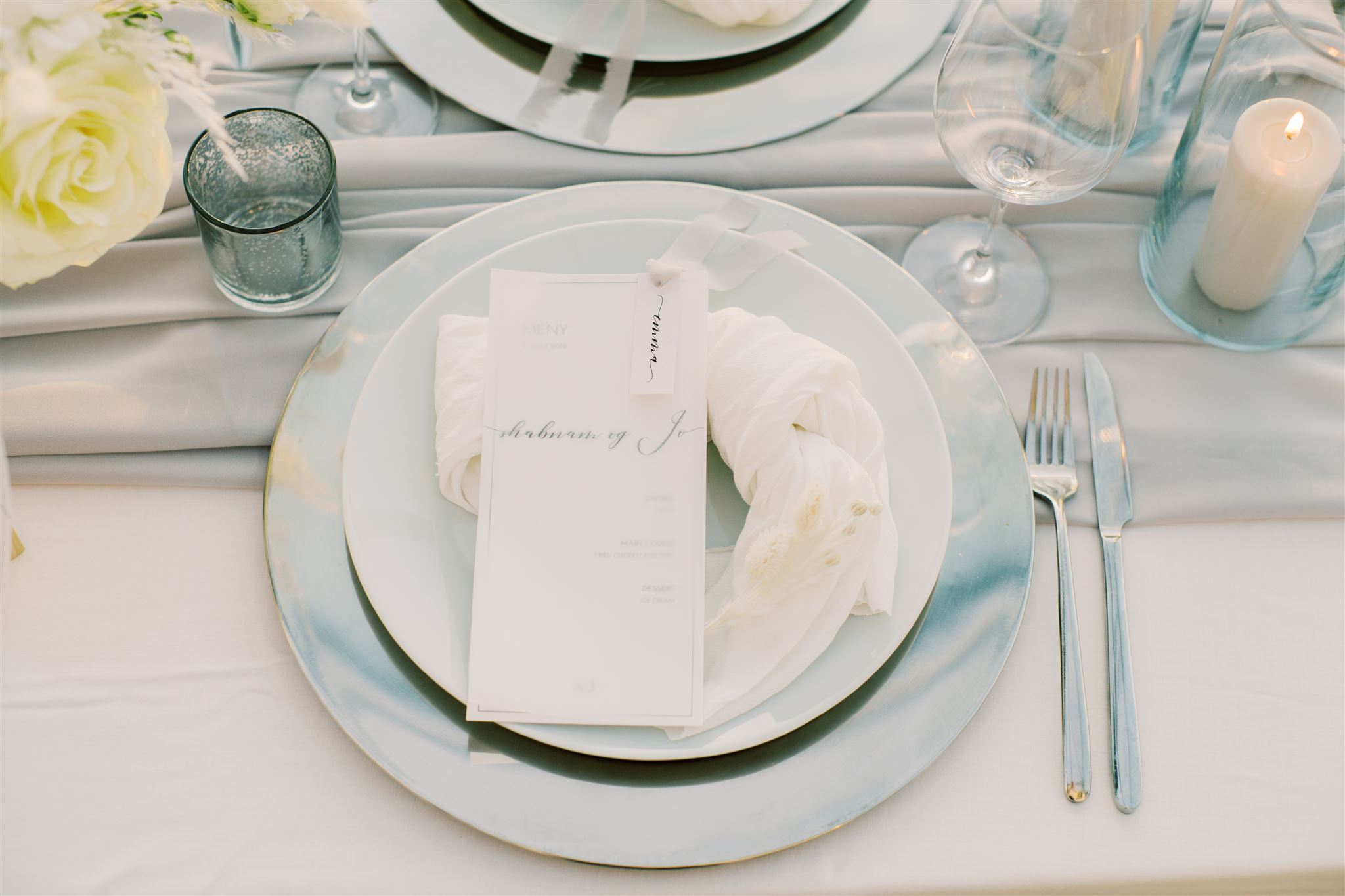 Moderne meny med grått silkebånd og grå løper til bordet med dekketallerken i sølv og hvite servietter.