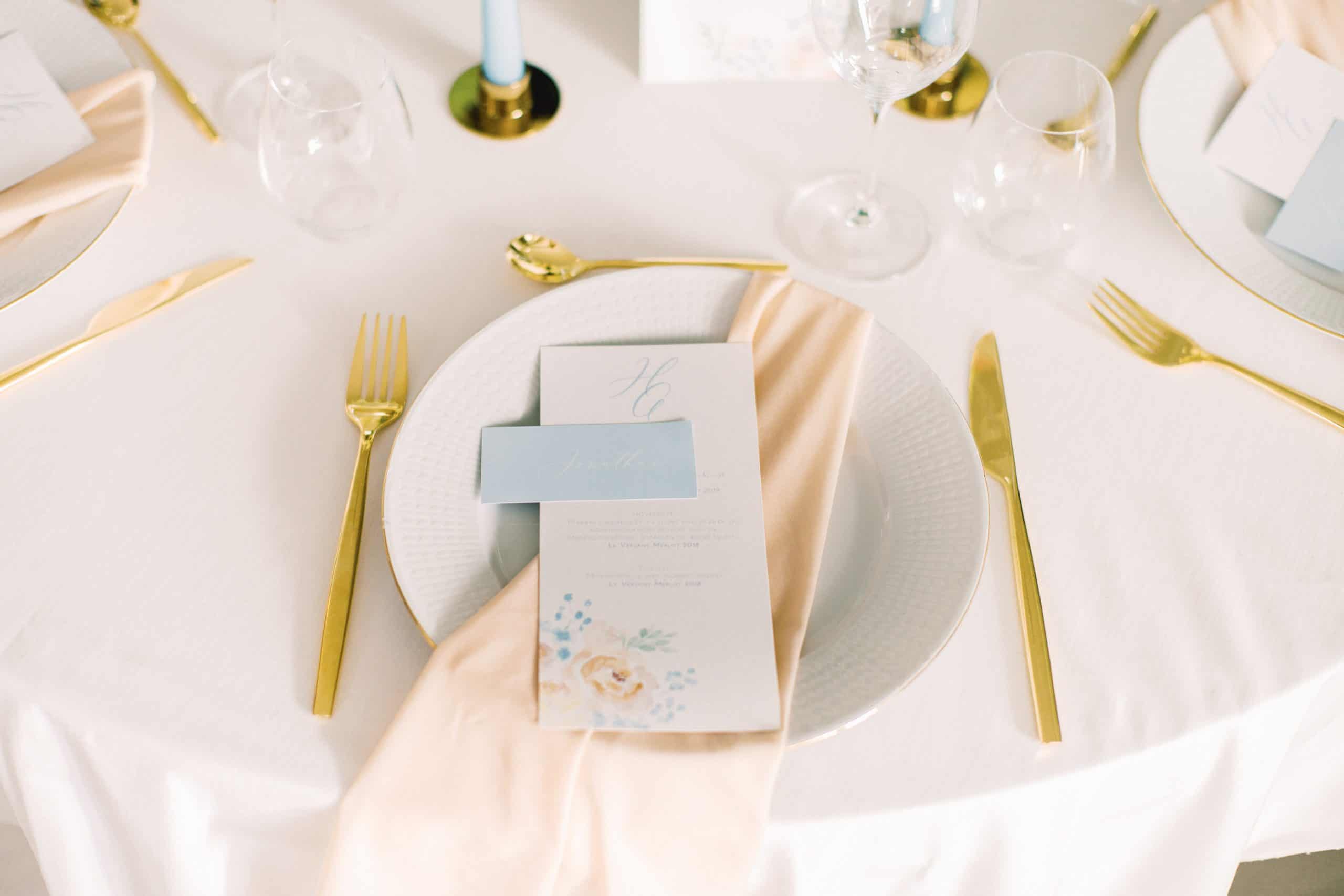 Runde tallerkener med lyseblå bordkort og gullbestikk