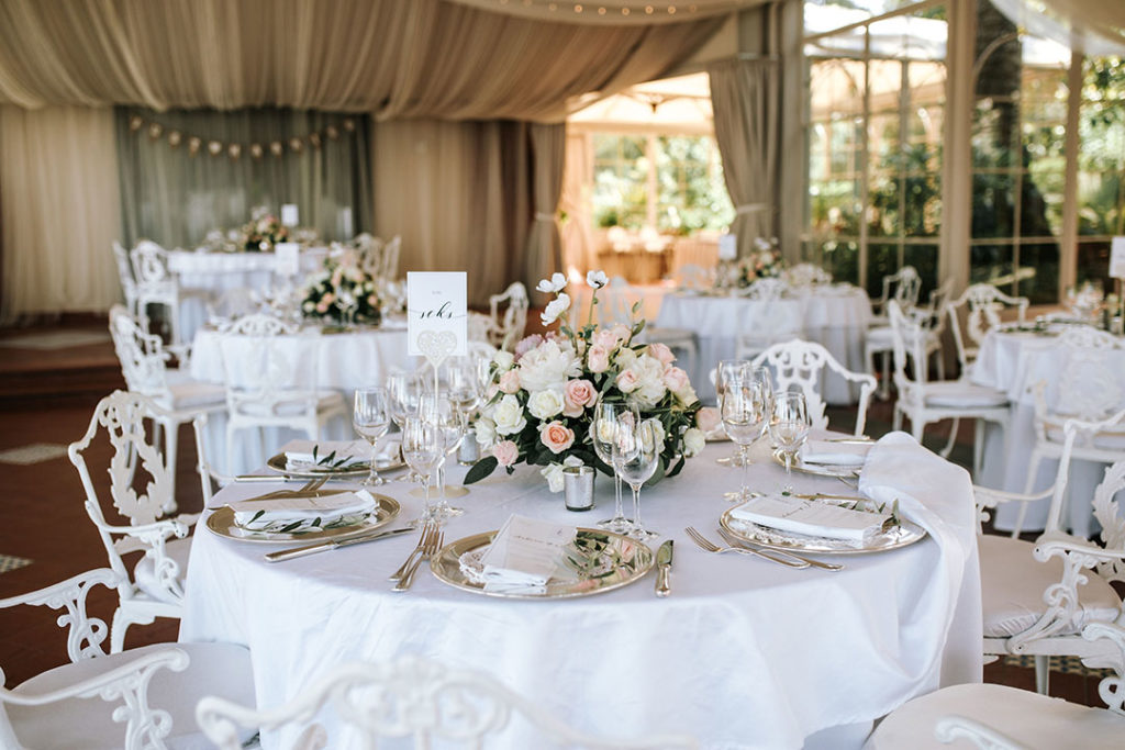 Bryllupsbord i Sorrento med elegante blomsterbuketter og hvite runde bord med hvite stoler.