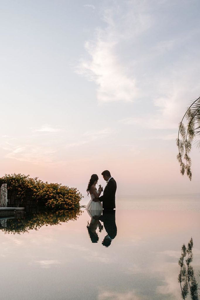 Brudepar i solnedgangen med havblikk i brudekjole og dress, med rosa himmel i Italia.